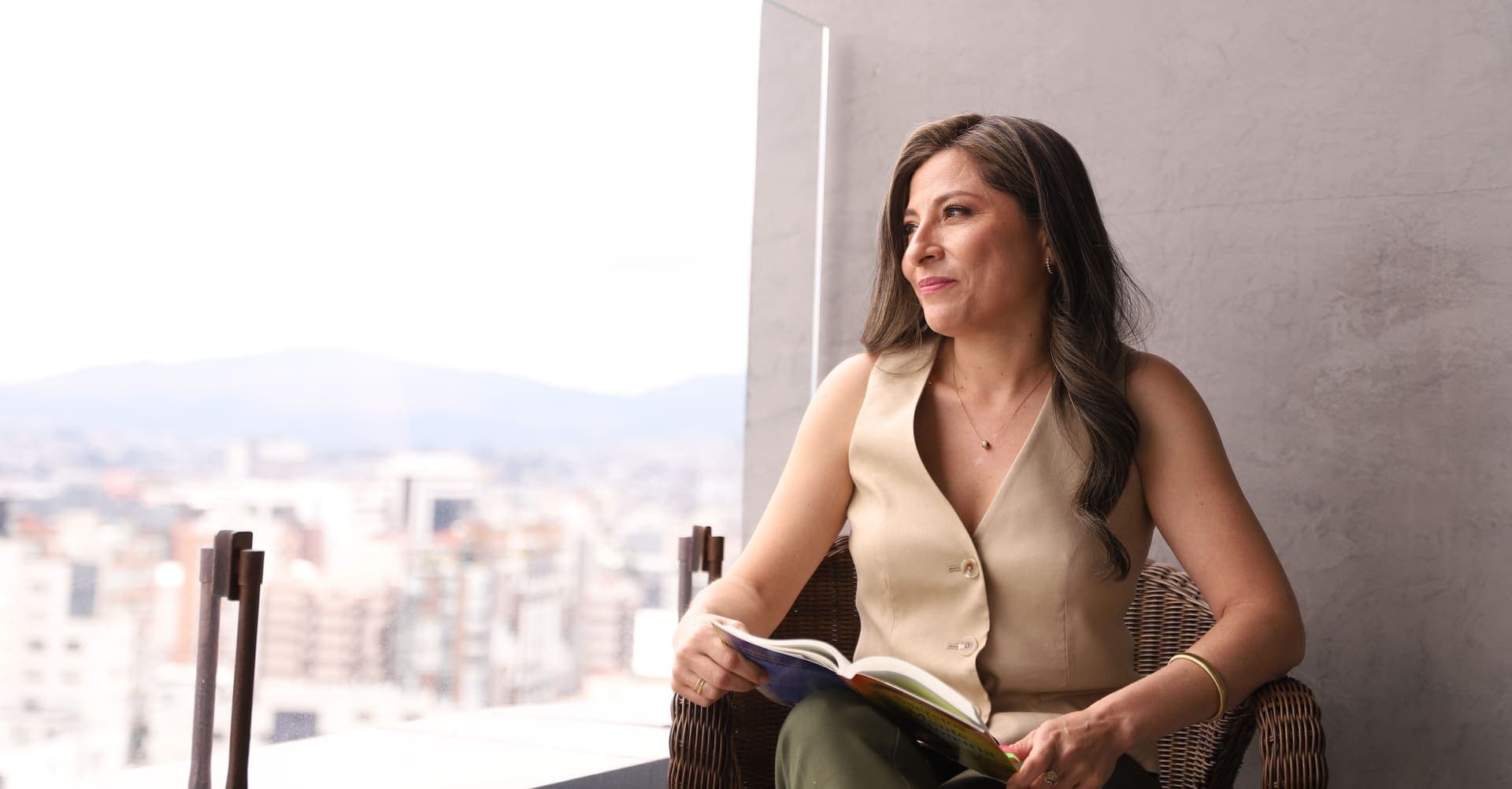 Katherine Gómez junto a la ventana, con un libro en las manos y la ciudad detrás